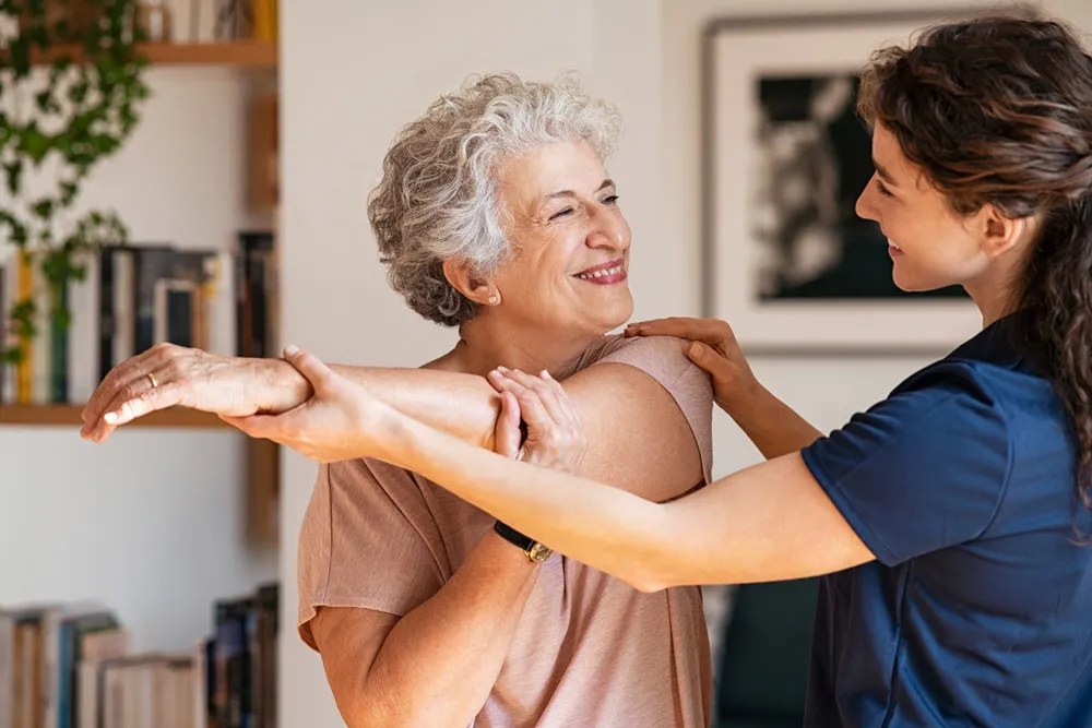 Young female physiotherapist guiding older lady with arm stretch.